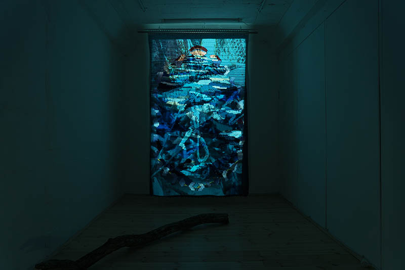 View of the exhibition 'Are we feeling blue_ An ode to the sea' in June 2021, Weaving (170cm x 250cm), tree brunch and video projection