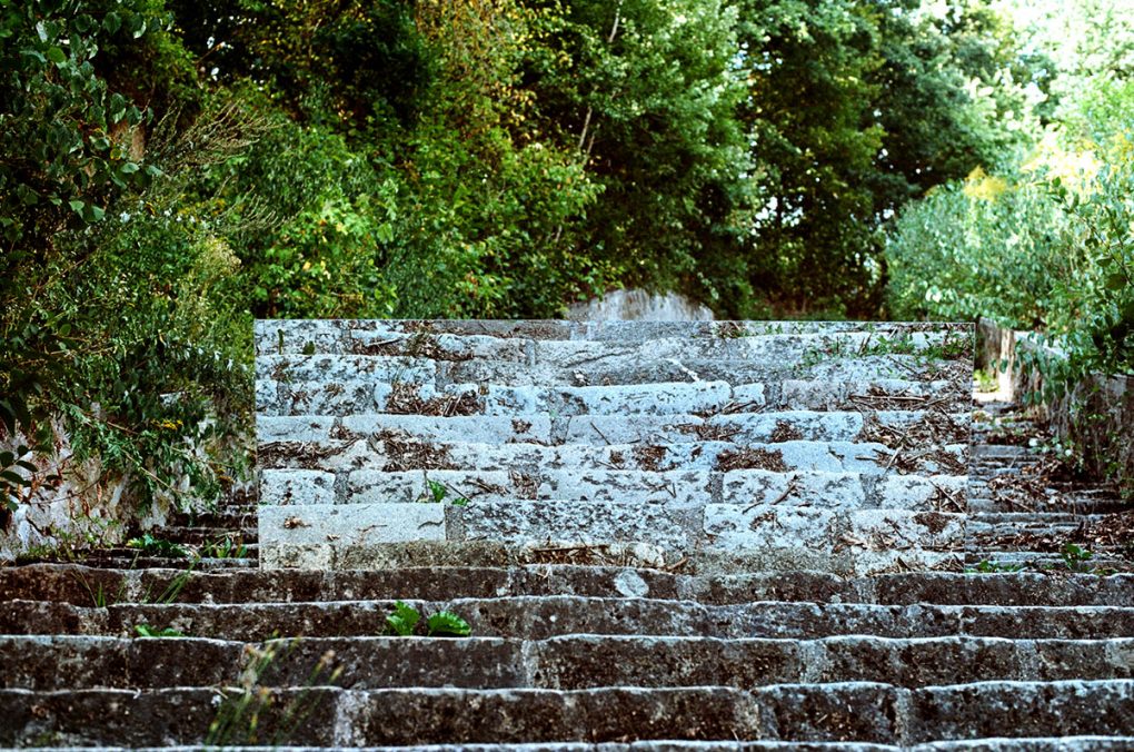 Die Wiederholung_5, 2018 Analoge Fotografie, Dibond, 120 × 80cm  Ort: Todesstiege Technik: Das Negativ wurde vor Belichtung gekocht. Konzept: Auf der Todesstiege wurde ein Spiegel positioniert, um die Treppen optisch ins nicht enden Wollende zu verlängern. Doch es wird ein anderer Blick eröffnet, nicht die Unendlichkeit und das Spiegelbild sind zu erkennen, sondern die Selbsterkenntnis des Menschen wird hinterfragt. Eine Mahnung, dass alle Abbilder und Formen nur Reflexionen sind, um uns an die Geschichte zu erinnern. © Courtesy of the Artist & Galerie Michaela Stock