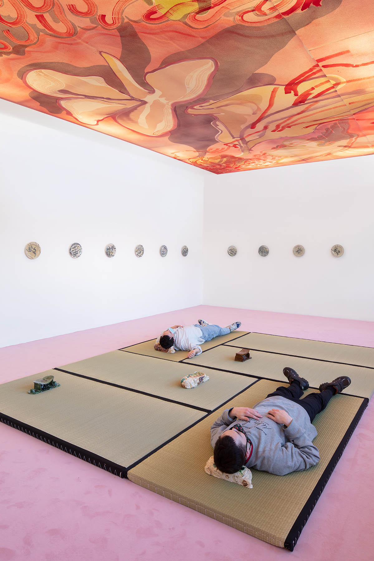 Installation view: Matthew Lutz-Kinoy. Window to The Clouds; Salon Berlin, Museum Frieder Burda Matthew Lutz-Kinoy, Wings of Flamingos, Camargue, 2020. Acrylic on canvas, 380 × 690 cm. Courtesy of the artist; Keramikos 3, 2019. Hand-painted set of 20 glazed ceramic plates. Courtesy of the artist and Mendes Wood DM São Paulo, New York and Brussels; Pillow In Cognac With Relaxed Figure, 2018; Pillow In The Form Of Reclining Child With Polkadots, 2018; Pillow In Green With Relaxing Figure, 2018; Pillow In The Form Of Reclining Child With Landscape, 2018; Pillow In The Form Of Reclining Child, Fishing Net, 2018. Glazed ceramics, dimensions variable. Courtesy of the artist and Fitzpatrick Gallery; Photo: Thomas Bruns